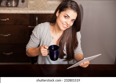 Top view of a beautiful young Hispanic woman having a cup of coffee for breakfast and using a tablet computer