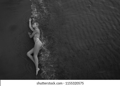 top view. Beautiful young woman with blond curly long hair and white swimsuit lies on wet sand of beach of sea. summer day. summertime. 