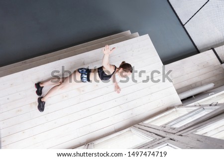 Top view - beautiful young woman athlete doing balance exercises standing on hand and leaning on feet on the podium next to the window in the white gym