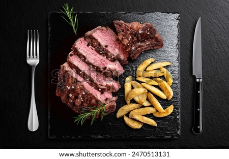 Top view of Beef steak and potatoes on black slate with cutlery