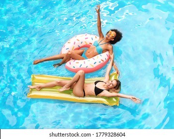 Top View Of Best Friends Floating On Lilo And Inflatable Ring At Outdoor Swimming Pool