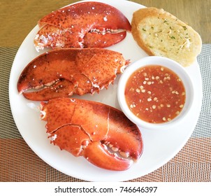 Top view of big lobster claws served on white plate with sauce and garlic bread