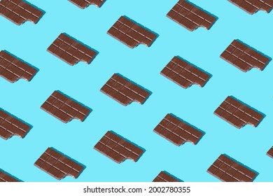 Top View Of Bitten Milk Chocolate Bar Pattern In Blue Background. Minimal Concept Of Sweet Food. Creative Candy Layout. Flat Lay.