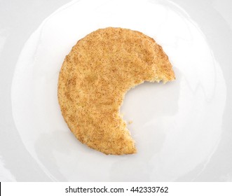 Top View Of A Bitten Snickerdoodle Cookie On An Off White Plate.