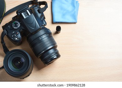 Top view of black digital camera, DSLR with lens, cleaning brush and cloth on wooden desktop with space for text.