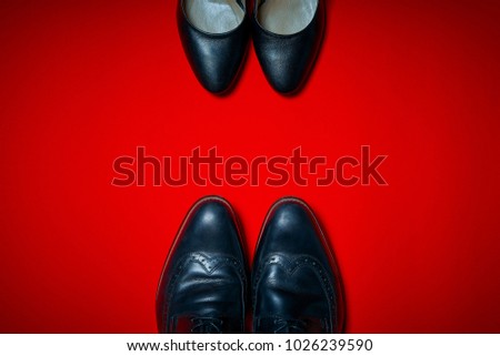 Top view of black high heels and men's shoes on an intense red background