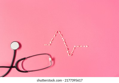 Top View Of Black Medical Stethoscope Adn Ekg Pattern Made Of Pills On The Pink Background.