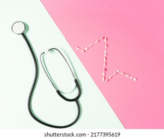 Top View Of Black Medical Stethoscope Adn Ekg Pattern Made Of Pills On The Pink Background.