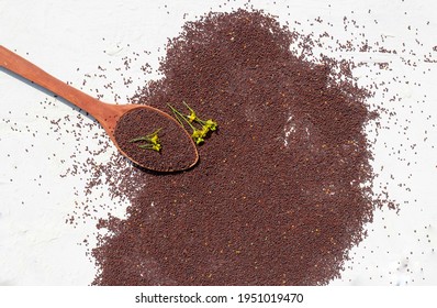 Top View Of Black Mustard Seeds With Mustard Flower In A Wooden Ladle On White Background In Horizontal Orientation