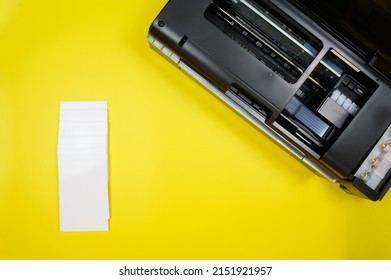 Top View Of A Black Printer And A Stack Of Blank Sheets Of A6 Photo Paper On A Yellow Background, Mockup.Office Equipment.Copy Space. Mock-up.High Quality Photo