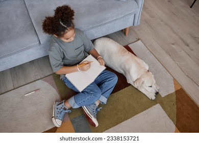 Top view at black teenage girl writing in diary while sitting on floor at home with white dog, copy space - Powered by Shutterstock