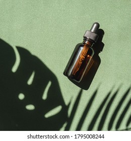 top view of Blank amber glass essential oil bottle with pipette on green background with tropical leaves shadows.