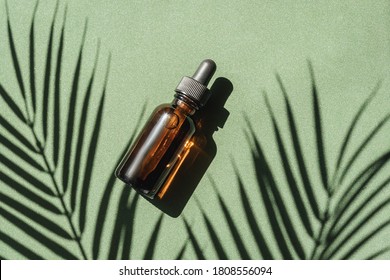 top view of Blank amber glass essential oil bottle with pipette on green background with tropical leaves shadows.