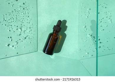 Top View Of Blank Amber Glass Face Serum Bottle With Pipette On Turquoise Background With Water Drops Shadow.