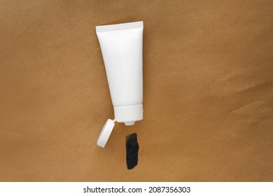 Top view blank label facial skincare white tube bottle with lid open product squeezed charcoal detox deep purifying creamy clay mask smear on eco friendly recyclable brown paper bag texture background