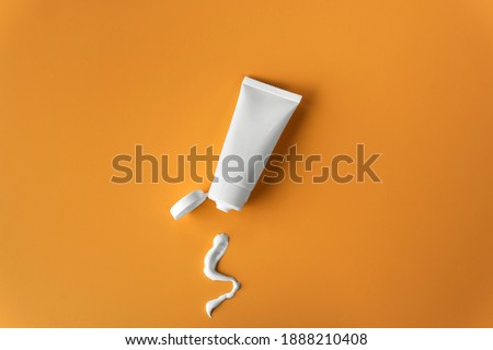 Top view blank label facial skincare white tube bottle with lid open product squeezed lotion or cream texture on plain solid orange background