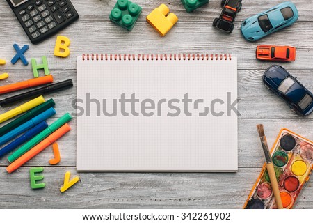 Top view of blank notebook, school supplies and toys on a white wooden desk.
