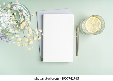 Top view blank paper Notebook, flowers, water with lemon and pen. Desktop mock up, Flat lay of green working table background with office equipment, mockup greeting card