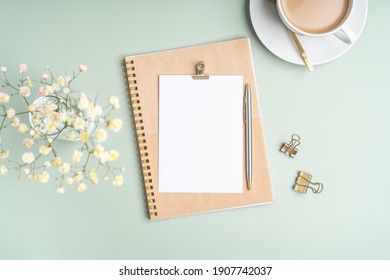 Top view blank paper Notebook, flowers, golden paper binder clips, cup of coffee and pen. Desktop mock up, Flat lay of green working table background with office equipment, mockup greeting card - Powered by Shutterstock