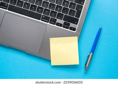 Top view of blank post-it stuck on laptop on blue table