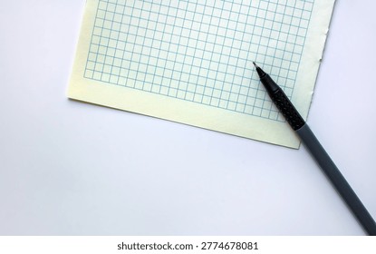 A top view of a blank sheet of grid paper with a pen. Isolated on a white background. Space for text.