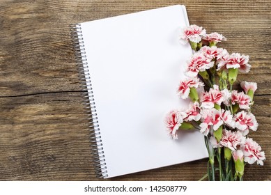 Top View Of Blank Sheet Of Notebook And Red And White Carnation Flowers On Rustic Brown Wooden Table. Copy Space.