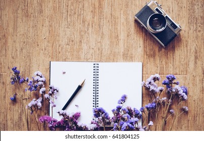Top view of blank space notebook paper and vintage camera on wooden texture with flower 