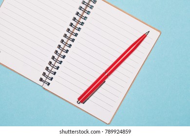 Top view blank spiral notebook and red pen on blue pastel color background with space. Blank writing pad for ideas and inspiration on colored background
