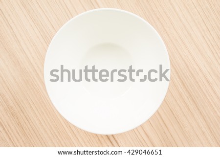 Top view of blank white bowl on a wood background.