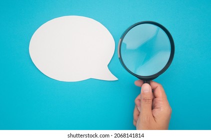 Top view of a blank white speech bubble and hand holding a magnifying glass on a blue background. - Shutterstock ID 2068141814