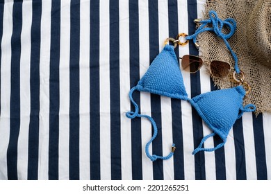 Top View Of Blue Bikini, Sunglasses  And Panama Hat On The Beach Blanket For Picnic On The Beach. Summer Vacation, Summer In Holiday Concept.