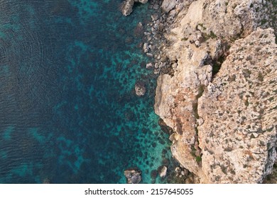 A top view of a blue ocean and a rocky cliff in daylight - Shutterstock ID 2157645055