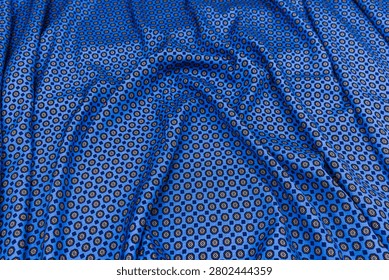 Top view of blue patterned necktie fabric with decorative geometric and floral motifs. Detailed textile texture with elegant folds, suitable as a fashion or luxury background.