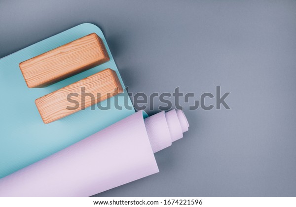 Top view of blue pink yoga mat and two wooden\
blocks on pastel grey background. Yoga pilates  Sport concept. Flat\
Lay. Copy space.