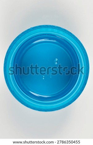 Top view of a blue plastic measuring cap filled with clear liquid laundry detergent showing small bubbles isolated on a plain background.