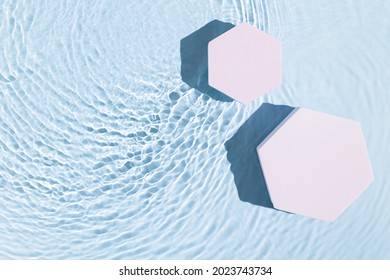 Top view of blue transparent clear calm water surface. Texture with splashes and bubbles with pink podium. Trendy abstract summer nature background for product presentation. Flat lay cosmetic mockup