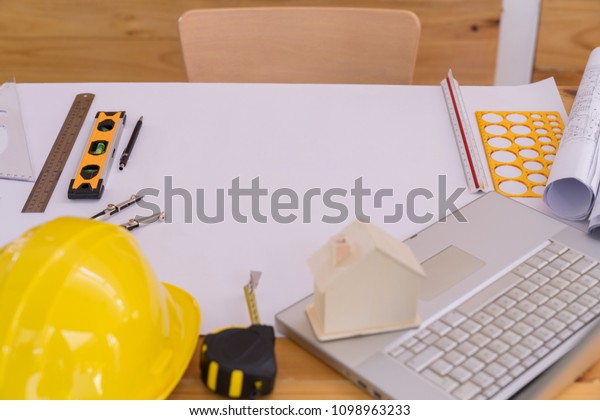 Top view of\
Blueprints, helmet, laptop, pencil, dividers, smartphone and\
engineer equipment on working\
desk.