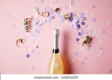 Top View Of Bottle Of Champagne And Confetti Pieces On Pink Surface