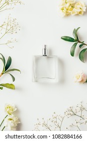 top view of bottle of perfume surrounded with flowers and green branches on white