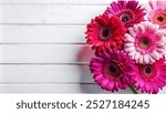 A top view of a bouquet of pink and red gerbera flowers on a white wooden table, with space for text.