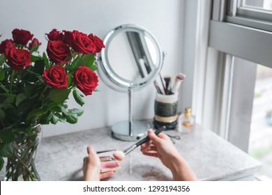 Top View, Bouquet Red Roses, Round Mirror, Female Hands Holds Makeup Brush And Blush On The Marble Vanity Table. Mothers Day Background