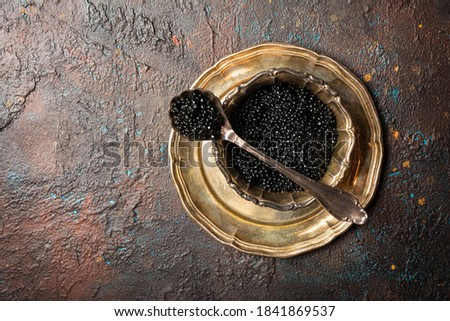Top view of bowl with appetizing black caviar and vintage silver spoon on dark concrete background with copy space