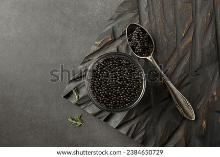 Top view of bowl with appetizing black caviar and spoon on dark concrete background with copy space