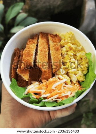 Top view of a bowl filled with chicken katsu, a  Japanese dish of crispy chicken breast fillet breaded with flour, egg, and Japanese panko breadcrumbs served with scrambled egg and vegetable salad