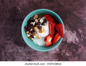 Top View Of A Bowl With Plain Greek Yogurt And A Candy Trail Mix Plus Strawberries On A Marron Tabletop.