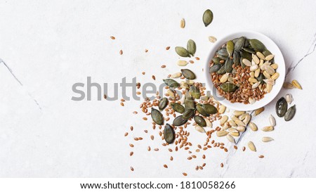 Top view of bowl with pumpkin, sunflower and flax seeds for healthy nutrition on white marble background with copy space