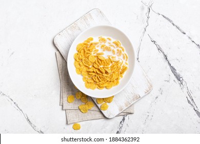 Top view of bowl with sweet corn flakes and milk for breakfast on white marble background