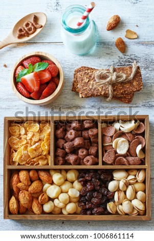 Top view of box with assorted cereal, nuts and raisin with homemade cereal bar, strawberry and milk. Healthy breakfast concept.