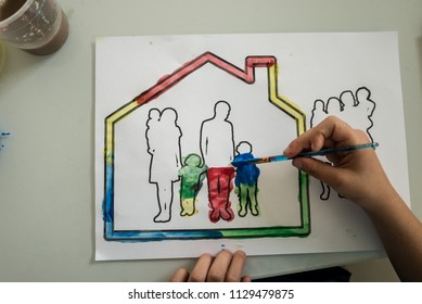 Top View Of A Boy Painting A Picture Of A Family In A House With Colourful Water Colour Paints.