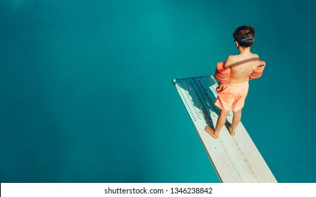Top view of boy standing on spring board learning to dive during swimming class on a summer day. Boy learning swimming at outdoor pool.